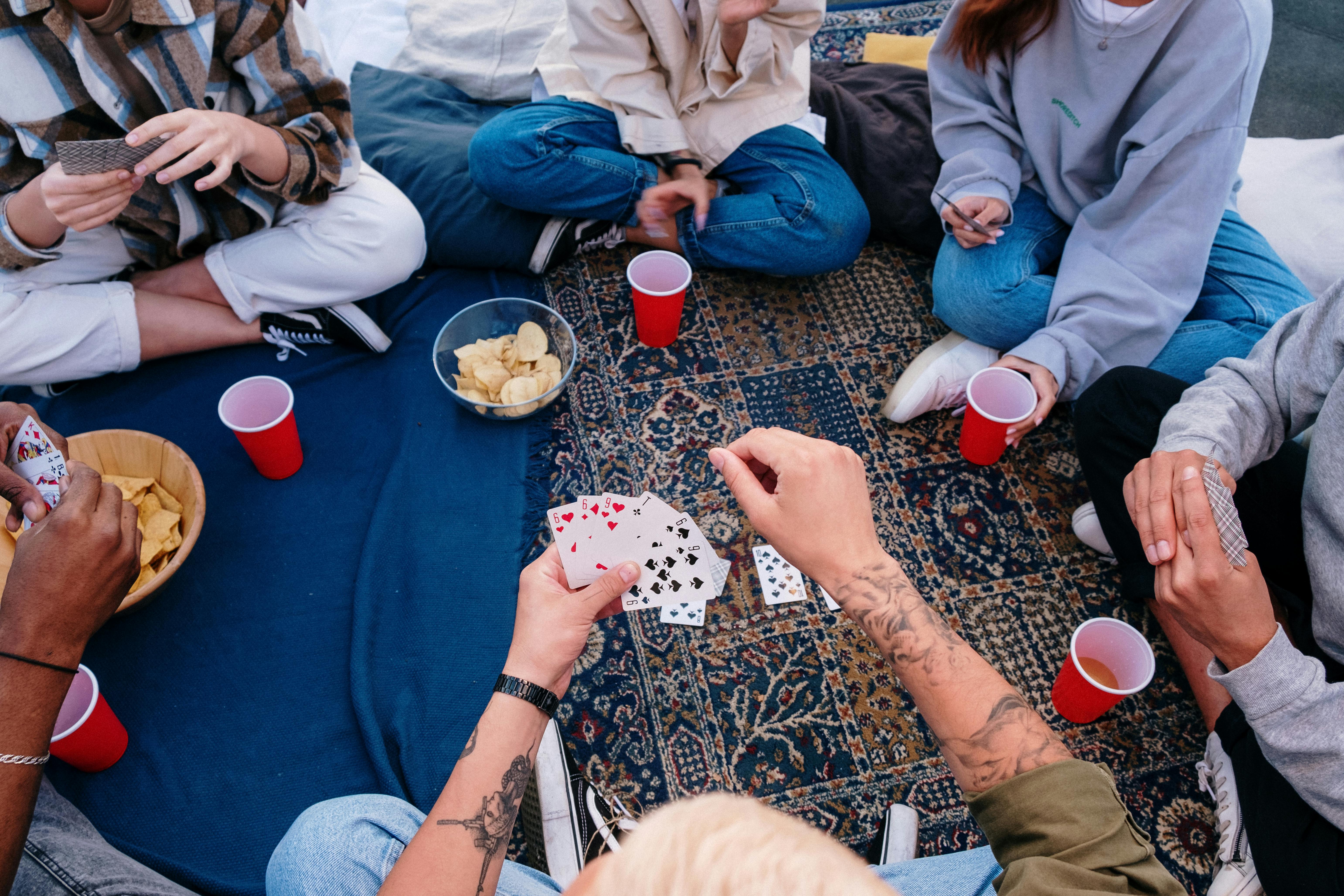 Friends enjoying a card game outdoors on a picnic blanket, sharing snacks and drinks.